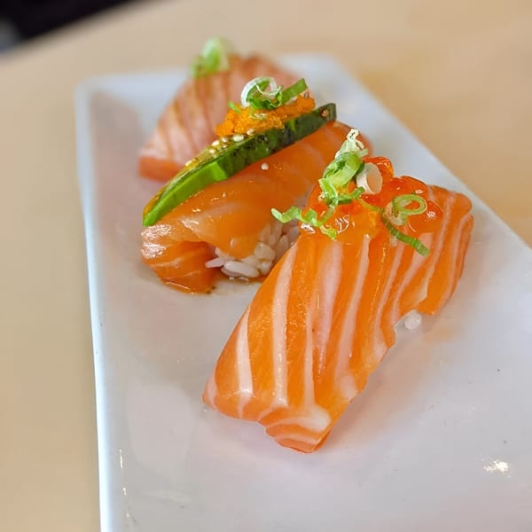 Three pieces of Mama M Sushi salmon nigiri with roe, avocado, and green onions on a white plate.