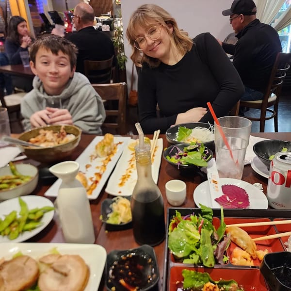 A family enjoys a meal at Mama M Sushi, with various sushi dishes and drinks on the table.