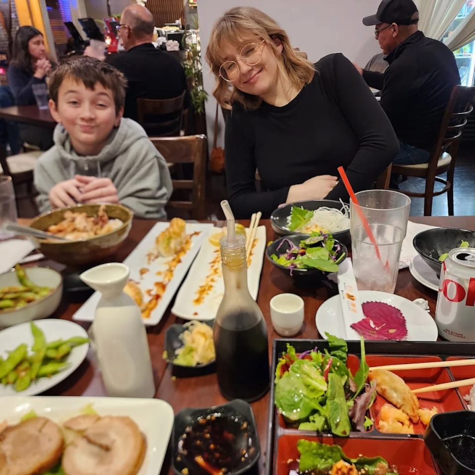 A family enjoys a meal at Mama M Sushi, with various sushi dishes and drinks on the table.