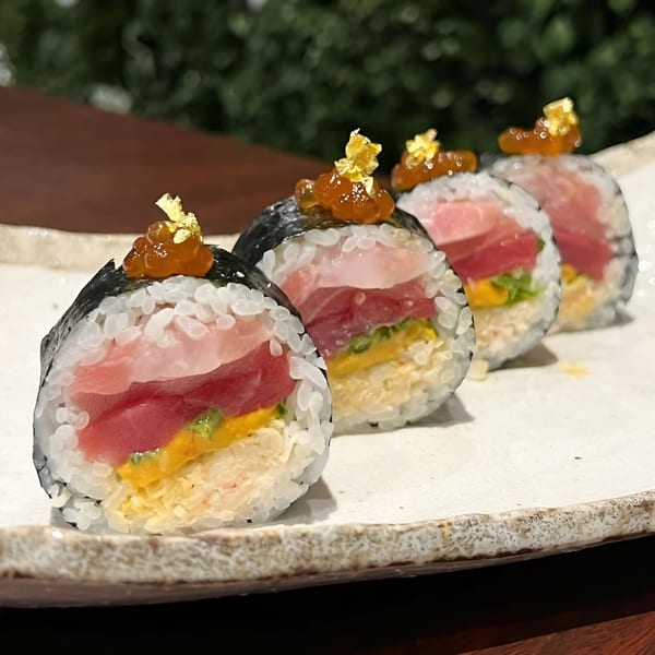 Four Mama M Sushi rolls with tuna, yellow filling, roe, and gold flakes on a white plate.