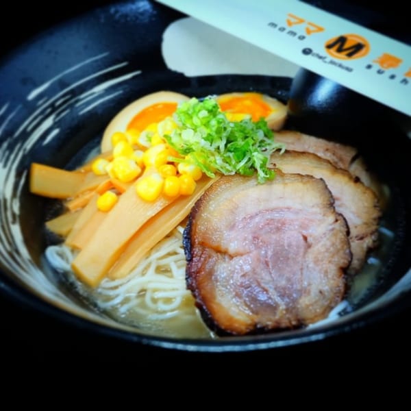 A bowl of ramen with pork, corn, bamboo shoots, green onions, and a soft-boiled egg.