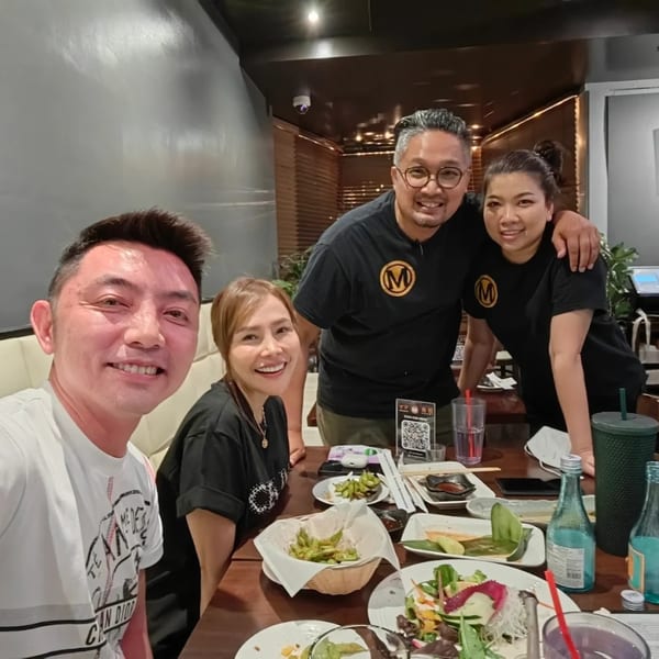 Four smiling people at a table with plates of sushi, edamame, and drinks at Mama M Sushi.